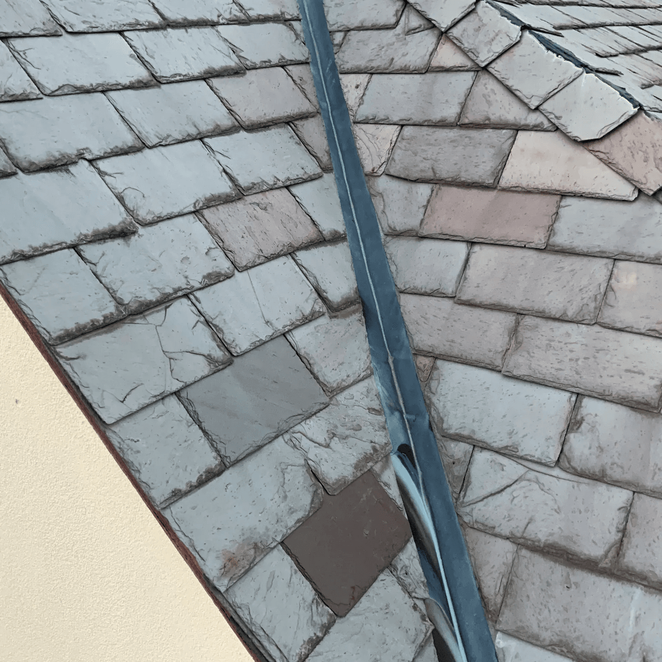 Slate roof meeting at a metal-lined valley, with several cracked slates on one side